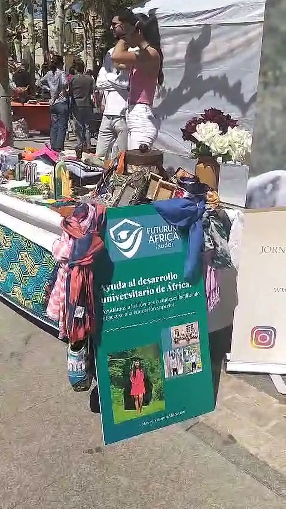 Cartel de AUDE junto a la mesa del puesto en el mercadillo de primavera